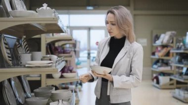 Mutfak malzemeleri satan bir dükkanda genç bir kadın ev için yeni yemekler seçiyor. Alıcı plakaları inceler. Ev eşyaları.