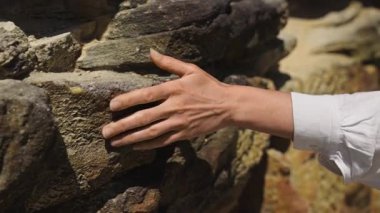 Kadın eli kaba kumtaşı dokusuna nazikçe dokunuyor, organik desenler ve doğal yüzeylerle doğaya bağlanıyor. Toprak tonlar ve dokunsal hisler. Doğa