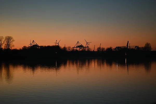Evening mood besides a river against a container port and a beautyful sunset