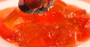 Pembe arka planda bir tabakta meyveli jelatin jöle. Kaşıkta jöle parçaları.