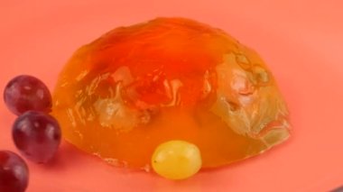 Pembe arka planda çok renkli jelatin jöleye düşen üzümler. Yavaş çekim.
