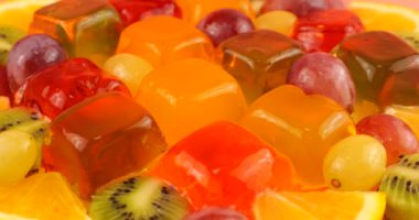 Üzümlü, portakal dilimli ve kivili, renkli böğürtlen jölesinin üzerine düşen portakal suyu damlaları..