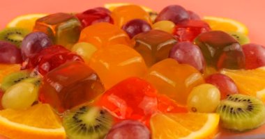 Çok renkli bir böğürtlen jelatin jölesinin üzerine portakal ve kivi dilimleri dökülen üzümler..
