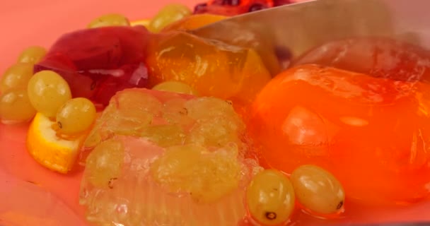 マルチカラーのベリーゼラチンゼリーのナイフブドウとピンクの背景にオレンジのスライスで切断 — ストック動画