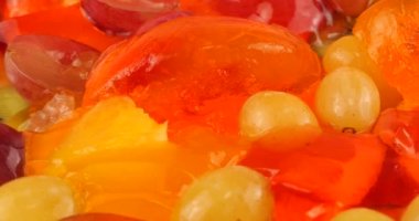 Çok renkli bir böğürtlen jelatin jölesinin üzerine portakal ve pembe arka planda kivi dilimleri dökülen üzümler..