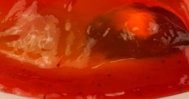 Pembe arka planda beyaz bir tabakta çilek soslu çok renkli jelatin jöle. Kaşıkta jöle parçaları.