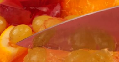 Çok renkli bir böğürtlen jelatin jölesinin, pembe arka planda üzümlü ve portakal dilimli bıçağıyla kesilmiş..