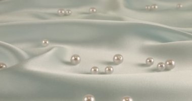 Beyaz kuğu tüyleri, incilerle birlikte soluk mavi ipeğe düşer. Yavaş çekim.