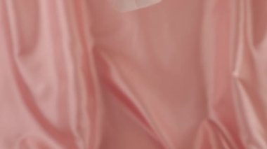 Beyaz kuğu tüyleri ipek renkli pembe arka plana düşer. Yavaş çekim.