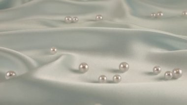 Beyaz kuğu tüyleri, incilerle birlikte soluk mavi ipeğe düşer. Yavaş çekim.