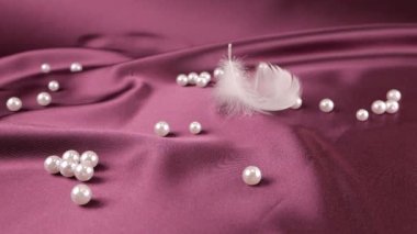 Beyaz kuğu tüyleri menekşe erik ipeğine ve incilere düşer. Yavaş çekim.