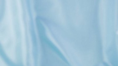 Beyaz kuğu tüyleri ipek renkli mavi arka plana düşer. Yavaş çekim.