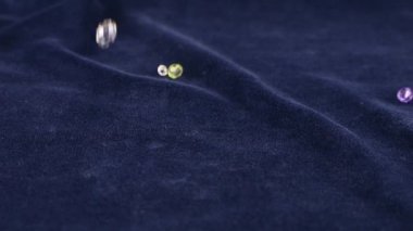 Multi-colored transparent jewelry crystals and rock crystal fall on blue velvet. Slow motion.