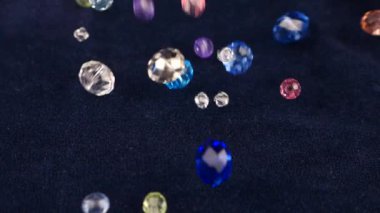 Multi-colored transparent jewelry crystals and rock crystal fall on blue velvet. Slow motion.