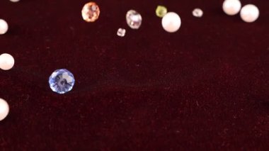 Multi-colored transparent jewelry crystals and white pearls fall on burgundy velvet. Slow motion.