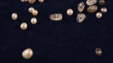 Natural pearls, quartz, rock crystal fall on dark blue velvet. Slow motion.