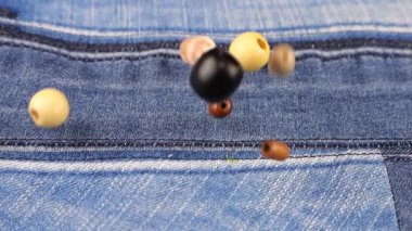 Decor elements made of natural materials, wood and shell beads fall on denim. Slow motion.