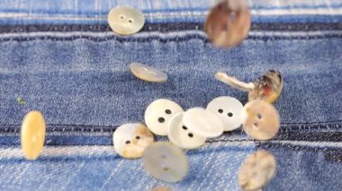 Natural mother of pearl buttons fall on denim. Slow motion.