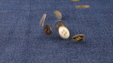 Natural mother of pearl buttons fall on denim. Slow motion.