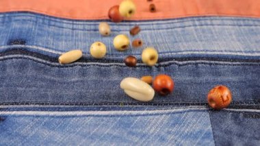 Decor elements made of natural materials, wood and shell beads fall on denim. Slow motion.