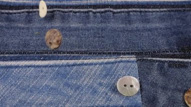 Natural mother of pearl buttons fall on denim. Slow motion.