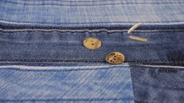 Natural mother of pearl buttons fall on denim. Slow motion.