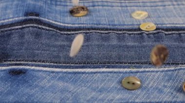 Natural mother of pearl buttons fall on denim. Slow motion.