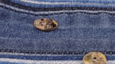 Natural mother of pearl buttons fall on denim. Slow motion.