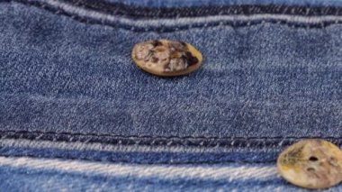 Natural mother of pearl buttons fall on denim. Slow motion.