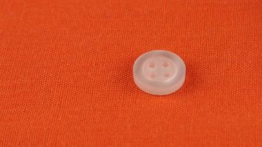 Plastic multi-colored buttons fall on an orange cotton fabric.