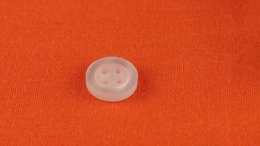 Plastic multi-colored buttons fall on an orange cotton fabric.