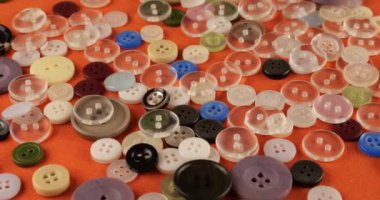 Plastic multi-colored buttons on an orange cotton fabric.
