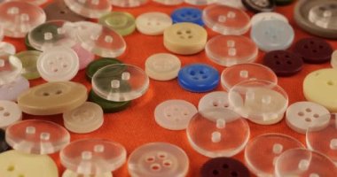 Plastic multi-colored buttons on an orange cotton fabric.