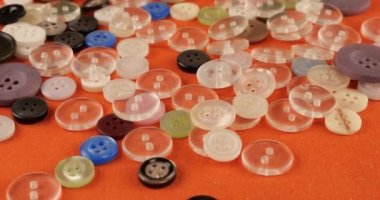Plastic multi-colored buttons on an orange cotton fabric.