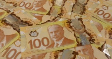 Falling Canadian coins on 100 dollar polymer banknotes with a portrait of Robert Borden.