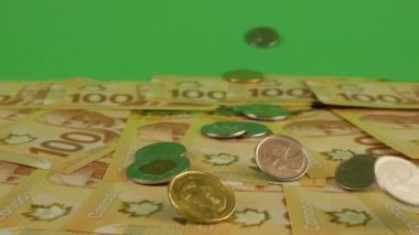 Falling Canadian coins on 100 dollar polymer banknotes with a portrait of Robert Borden. Slow motion. Shooting on a green background.
