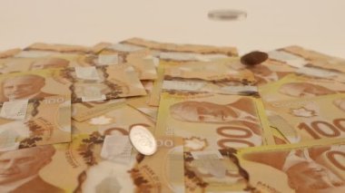 Falling Canadian coins on 100 dollar polymer banknotes with a portrait of Robert Borden. Slow motion.