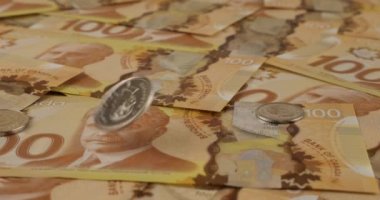 Falling Canadian coins on 100 dollar polymer banknotes with a portrait of Robert Borden. Slow motion.