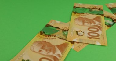 Falling Canadian 100 dollar polymer banknotes with a portrait of Robert Borden on a green background.