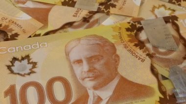 Falling Canadian coins on 100 dollar polymer banknotes with a portrait of Robert Borden.