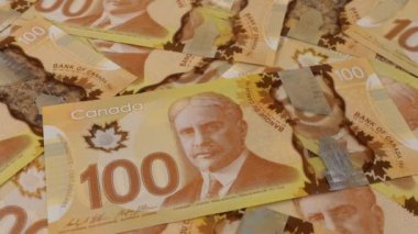 Falling Canadian coins on 100 dollar polymer banknotes with a portrait of Robert Borden.
