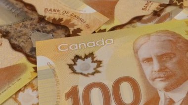 Falling Canadian coins on 100 dollar polymer banknotes with a portrait of Robert Borden.