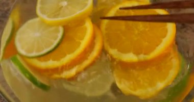 Cooking lemonade from citrus fruits in a glass container. Stir orange, ginger, lemon and lime wedges with wooden sticks.