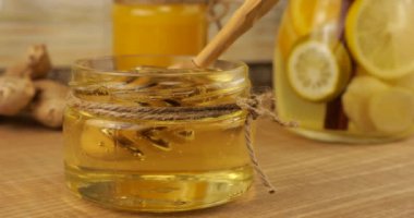 Honey flows from a spoon spindle into a jar of honey on the background of a jug of lemonade and ginger. Video on the topic of immunity and health.