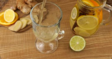 Cooking a drink of citrus and ginger to boost immunity. Lemonade is poured into a glass against the background of slices of orange, lemon, lime, ginger and a glass jug of lemonade.