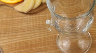 Cooking a drink of citrus and ginger to boost immunity. Lemonade is poured into a glass against the background of slices of orange, lemon, ginger and a glass jug of lemonade. Slow motion.