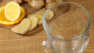 Cooking a drink of citrus and ginger to boost immunity. Lemonade is poured into a glass against the background of slices of orange, lemon, ginger and a glass jug of lemonade. Slow motion.