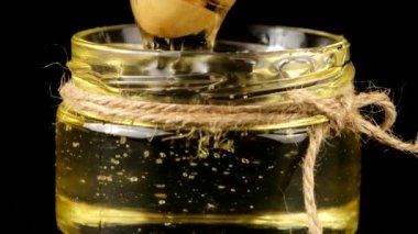 Honey flows down from a spoon spindle into a jar with honey on a black background.