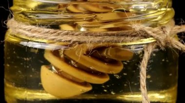 Honey flows down from a spoon spindle into a jar with honey on a black background.