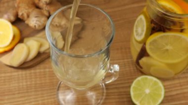 Cooking a drink of citrus and ginger to boost immunity. Lemonade is poured into a glass against the background of slices of orange, lemon, lime, ginger and a glass jug of lemonade.